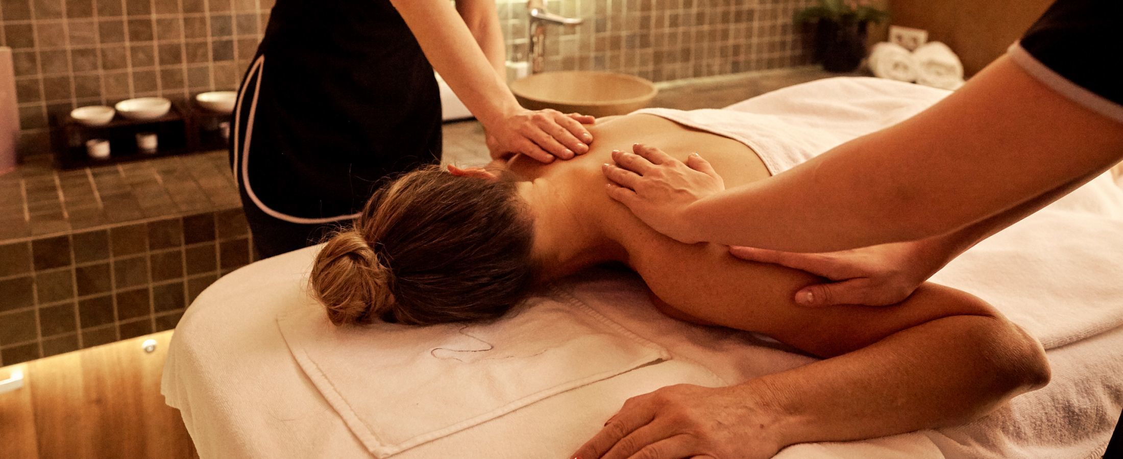 A woman getting a massage by 2 massage therapists, a 4 handed treatment